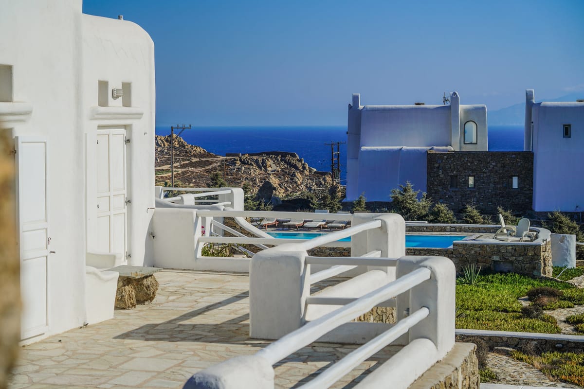 White villas above a pool, with the sea behind