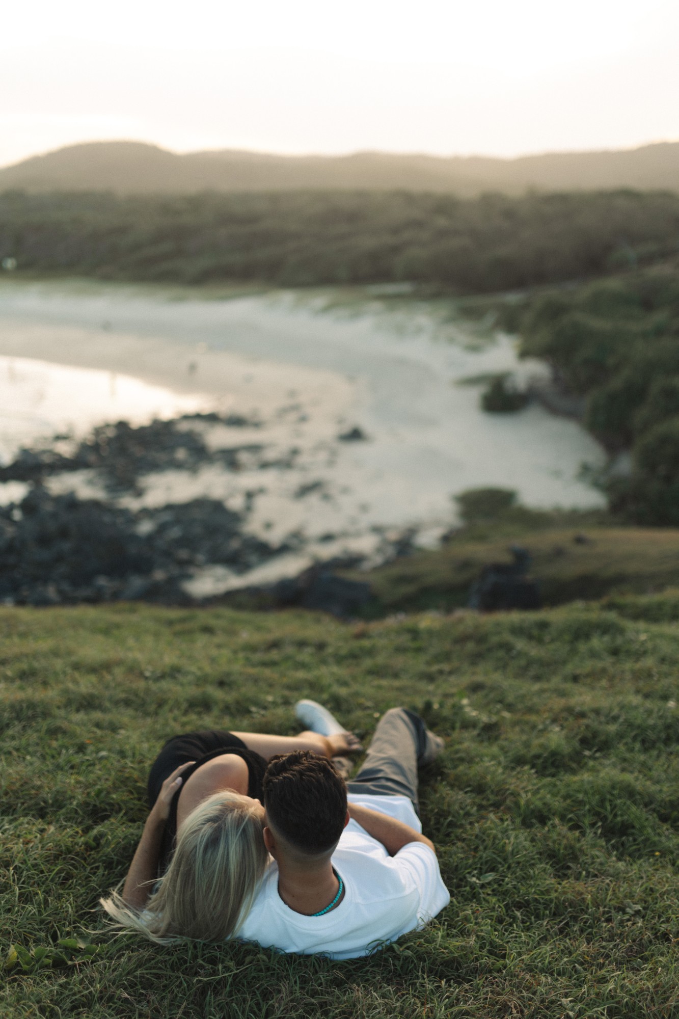 Sarah and Alex lying in the grass above a beach